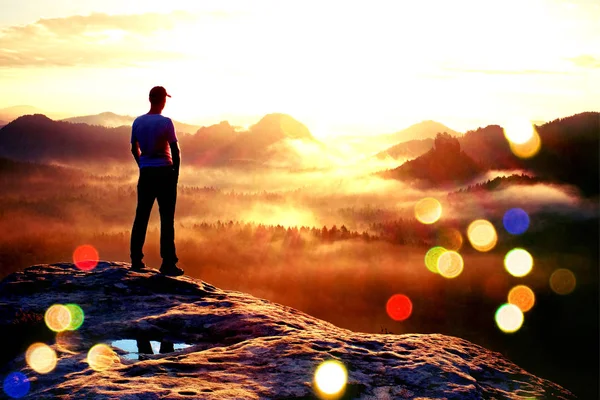 Filmové zrno. Turista v červené čepici stojí na vrcholu pískovcové skály v rock park říší a bdí nad údolím mlhavé a mlhavé ráno — Stock fotografie
