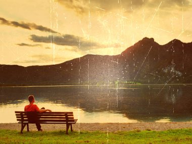 Film etkisi. Yalnız adam bir masmavi dağ Gölü yanında bankta üzerinde bacak oturur. Adam sakin ol ve Alpler yüksek doruklarına Gölü ayna yukarıda izle.