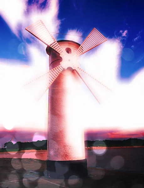 Film effect. White old lighthouse decorated as windmill by sea on rocky coast. Seascape and landscape — Stock Photo, Image