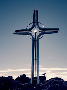 Yüksek kayalık dağ üzerinde çapraz Zirvesi dua. Çelik sanatsal haç Alp dağın zirvesinde