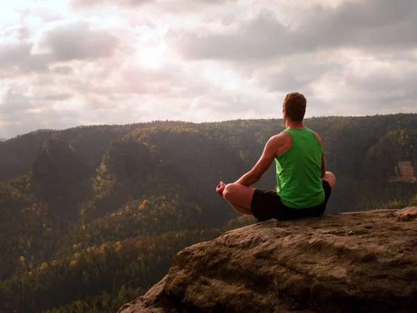 Man meditating in Lotus Pose on rocky cliff. Sportsman practicing Yoga on stone edge