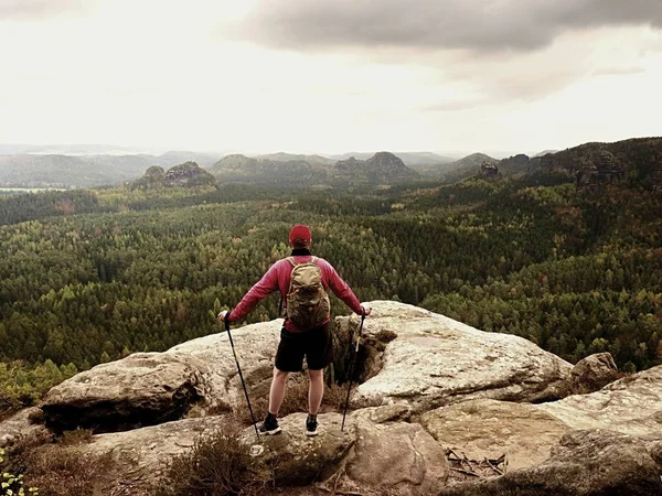 Man hiker with trekking poles and backpack on a top of a mountain. Traveler with Backpack