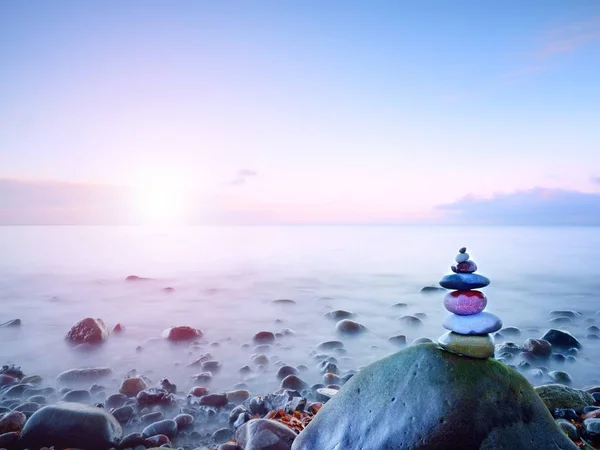 Pirámide de piedra balanceada en la orilla de agua azul del océano. Cielo azul en espejo de nivel de agua —  Fotos de Stock