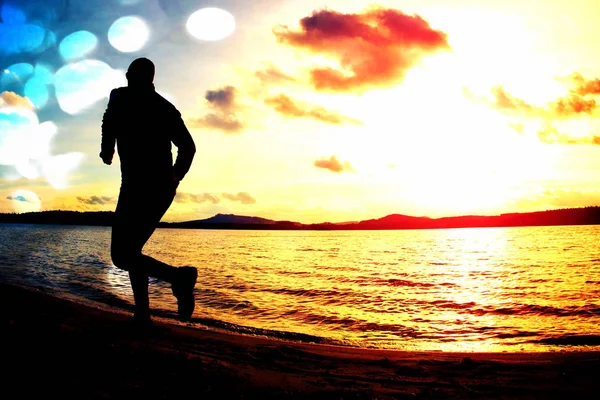 Grano de película. Silueta de hombre activo deportivo corriendo y ejercitándose en la playa al atardecer . — Foto de Stock