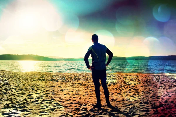 Grano de película. Silueta de persona en ropa deportiva y pelo corto en la playa viendo el sol de la mañana sobre el mar — Foto de Stock