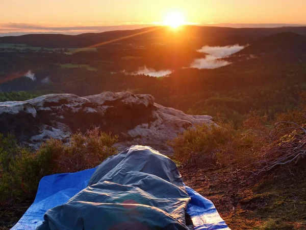 Beautiful awakening in a sleeping bag on  rock ledge. Birds are singing and Sun at horizon. — Stock Photo, Image