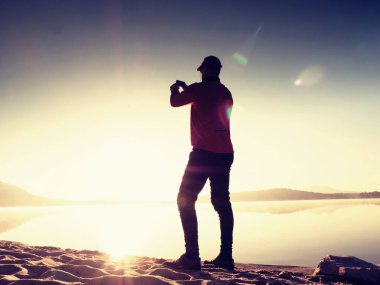 Onun arkasında da Denizi selfie fotoğraf çekmek için cep telefonu kullanarak deniz kenarında yalnız adam