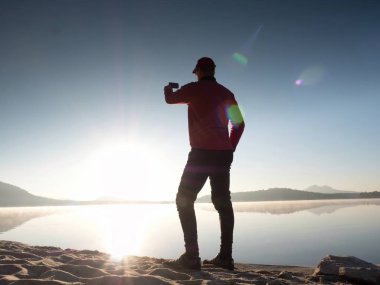 Selfie çekim plajda adam yan görünüm. Sıcak sabah göl üzerinde yükselen güneş.