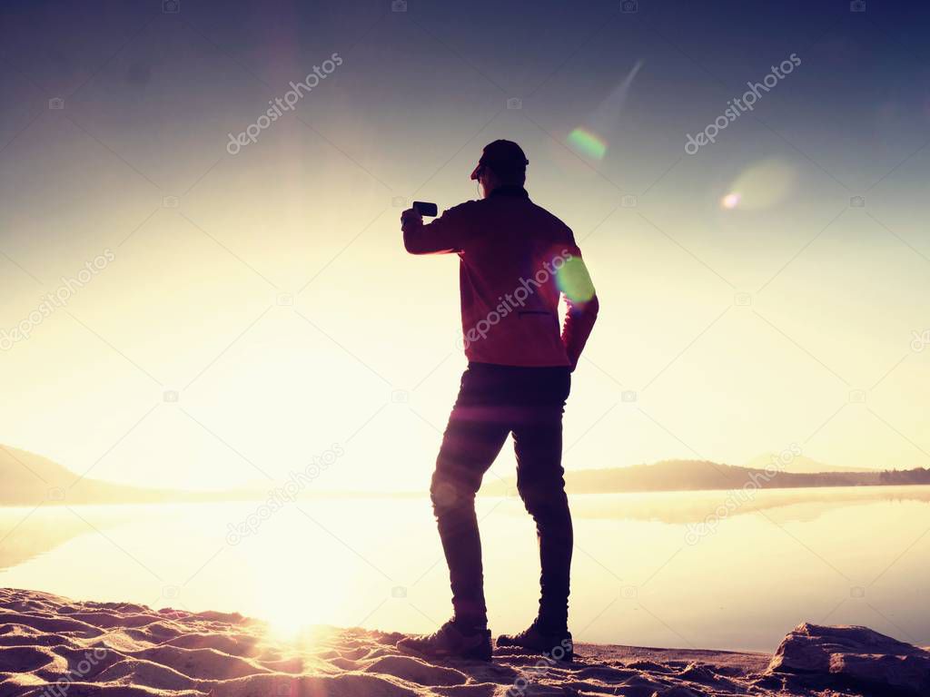 Alone man at the seaside using cell phone to take selfie photo with the sea behind him