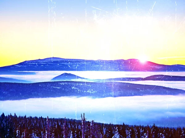 Film effekt. Rosa orange solen gå upp över dimmiga vintern berg, shinning dimma. Topparna av bergen ovanför krämig mist i dalen. — Stockfoto