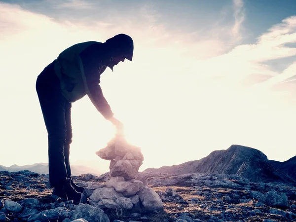 Man hiker is building pebbles pyramid. Stones on Alps mountain summit. Daybreak horizon — Stock Photo, Image