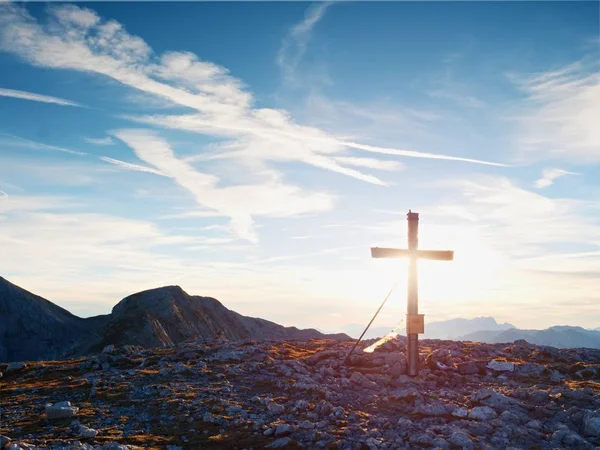 Modest wooden cross raised on rocky Alpine mountain summit . Sharp rocky peak. Gentle clouds  in blue sky. — Stock Photo, Image