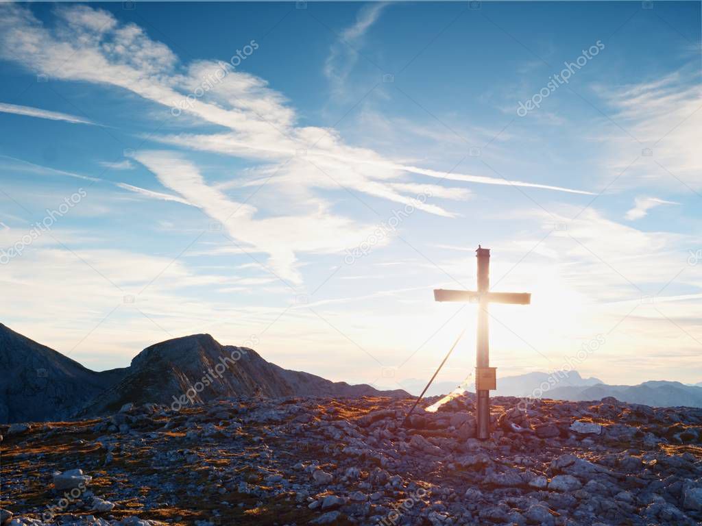 Modest wooden cross raised on rocky Alpine mountain summit . Sharp rocky peak. Gentle clouds  in blue sky.