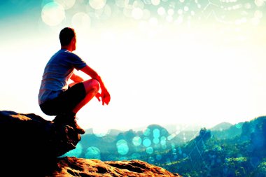 Film tahıl. Siyah pantolon ve gömlek genç hiker Cliff'in kenarında oturan ve puslu tepelik Vadisi körük için arıyorsunuz