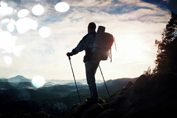 Grano filmato. Guida turistica sulla strada con palo in mano. Escursionista con zaino sportivo stare sul punto di vista roccioso sopra la valle nebbiosa. Sunny alba di primavera in montagne rocciose . — Foto Stock