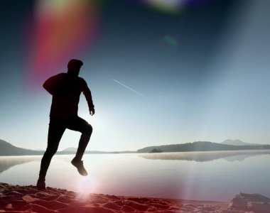  egzersiz ve göl kumsalda güneş doğarken uzanan bir adam. Sağlıklı bir yaşam tarzı. Yalnız genç fitness adam egzersiz sabah kumsalda