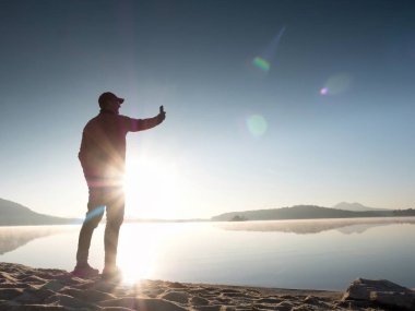 Selfie çekim plajda adam yan görünüm. Sıcak sabah göl üzerinde yükselen güneş.