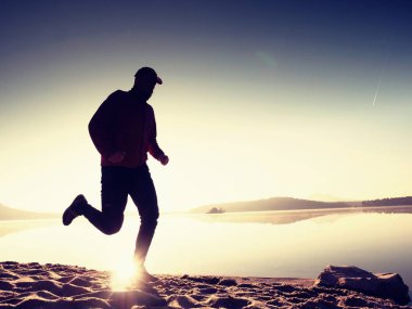 Gün doğumunda yansımayla plajda koşan bir çocuk. Açık gökyüzü ile Sabah Koyu Sahili.