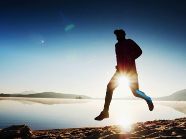 Gün doğumunda yansımayla plajda koşan bir çocuk. Açık gökyüzü ile Sabah Koyu Sahili.