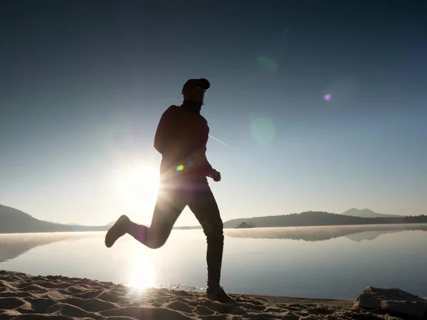 Hombre corriendo en la playa contra el telón de fondo de una hermosa puesta de sol. Arena de lago de montaña — Foto de Stock