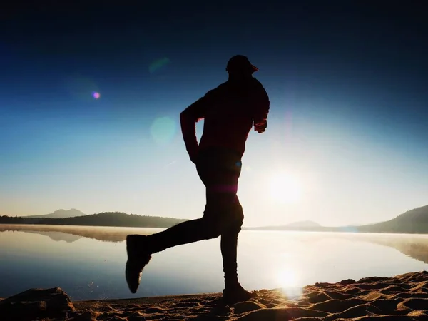 Ο άνθρωπος που τρέχει στην παραλία με φόντο ένα μαγευτικό ηλιοβασίλεμα. Άμμο της λίμνη βουνό — Φωτογραφία Αρχείου