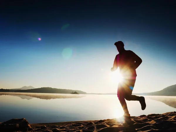 Muž běží na pláži nádherný západ slunce v pozadí. Písek z horské jezero — Stock fotografie