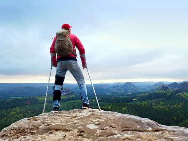 Homem deficiente com muletas fica em uma grande rocha e olhando para as montanhas no horizonte . — Fotografia de Stock