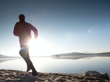 Gün doğumunda yansımayla plajda koşan bir çocuk. Açık gökyüzü ile Sabah Koyu Sahili.