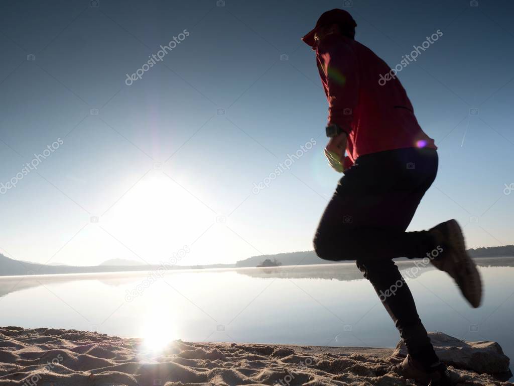 Tall fit man running fast by the sea on the beach. Powerful runner training outdoor in summer morning.