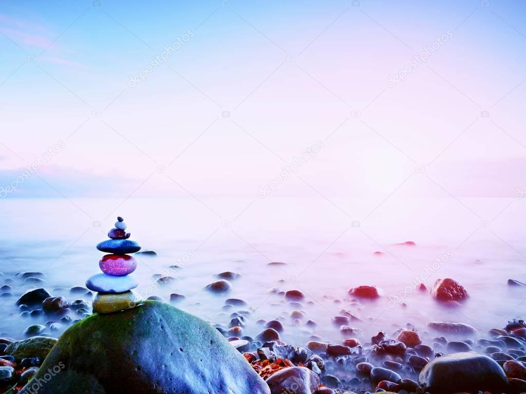 Balanced stone pyramide on shore of blue water of ocean. Blue sky in water level mirror