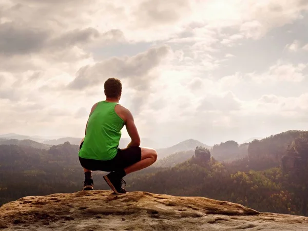 Yeşil singlet turist ve siyah şort bir kayaya çömelme pozisyonda zevk sahne.