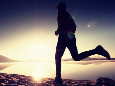 Gün batımında sahilde koşan bir adam. 