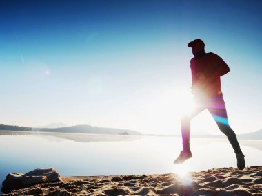 Gün batımında sahilde koşan bir adam. 