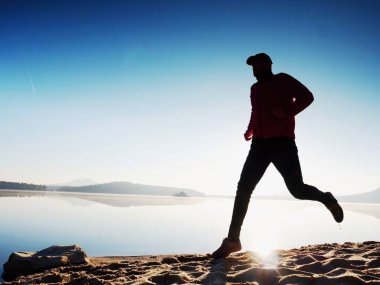 Gün batımında sahilde koşan bir adam. 