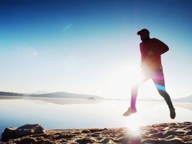 Gün batımında sahilde koşan bir adam. 