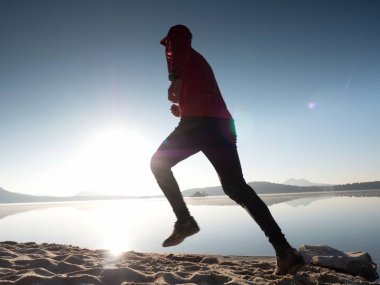 Gün batımında sahilde koşan bir adam. 