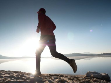 Gün batımında sahilde koşan bir adam. 