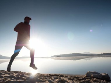 Gün batımında sahilde koşan bir adam. 