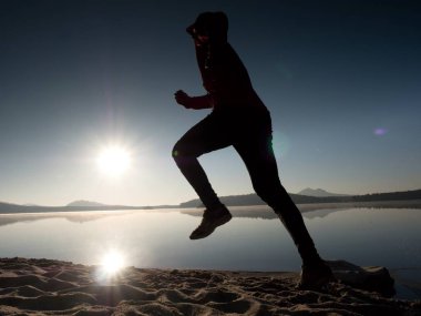 Gün batımında sahilde koşan bir adam. 