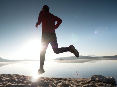 Gün batımında sahilde koşan bir adam. 