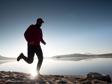 Gün batımında sahilde koşan bir adam. 