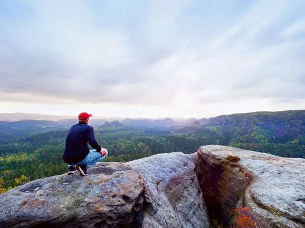 Muž v outdoor mikina džíny černé a červené víčko pobytu na konci prasklý skalnatého útesu — Stock fotografie