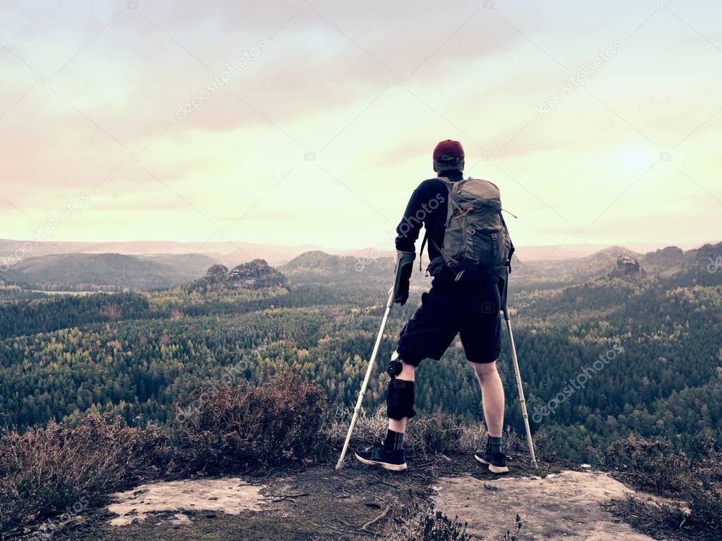 Disabled man on crutches on rock. Hurt knee in neoprene metal knee braces and man hold forearms crutches. 