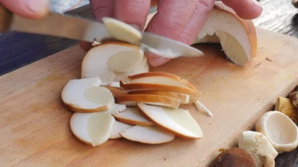 Pěkné hříbky jsou nakrájíme nožem na malé kousky na dřevěné prkénko. Muž ruce hřib řez na dřevěný stůl — Stock video