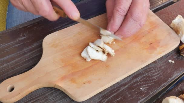 Nasekat čerstvé lesní houby. Detailní záběr záběr rukou s nožem řezání houby. Muž opatrně broušené hříbky na kuchyňské dřevěné desky — Stock video