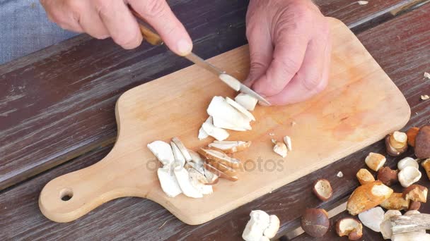 Подрібніть свіжі дикі гриби. Крупним планом постріл рук за допомогою ножа для різання грибів. Чоловік обережно порізав дикі гриби на дерев'яній дошці — стокове відео