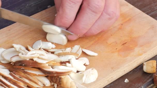 Close up shot of hands with a knife cutting mushrooms. Man hand carefully  cut wild mushrooms on a kitchen wooden board — Stock Video