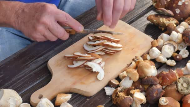 Cogumelos selvagens agradáveis são cortados com faca em pequenos pedaços em tábua de corte de madeira. Homem mãos cortar fatia de boleto na mesa de madeira — Vídeo de Stock