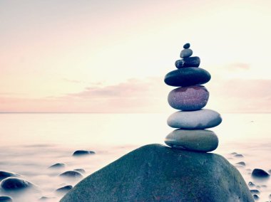 Mavi su okyanusun kıyısında taş pyramide dengeli. Su seviyesi ayna mavi gökyüzünde