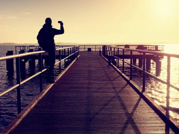 Der eine Mann mit Kapuze, der morgens vom hölzernen Hotelsteg auf das Meer blickt. — Stockfoto